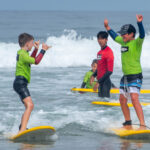 two kids surfing with instructor in background