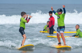 two kids surfing with instructor in background